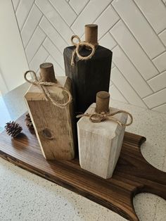 three wooden bottles tied with twine on top of a wood board next to a pine cone