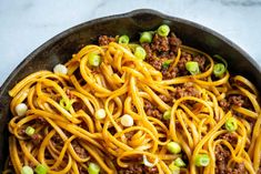 a skillet filled with spaghetti, ground beef and green onions on a marble surface