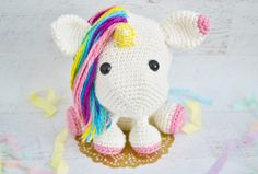 a crocheted stuffed unicorn sitting on top of confetti