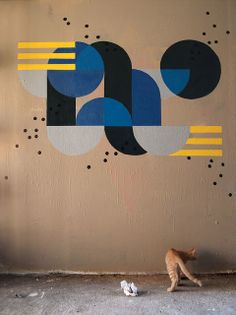 a cat walking past a wall with an abstract painting on it