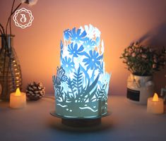 a blue and white lit up vase with flowers on it next to some pine cones