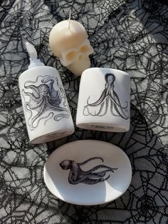 three cups with octopus designs on them sitting next to a candle and skull head decoration