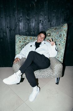 a man sitting on top of a leopard print chair next to a black wooden wall