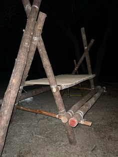 a wooden structure sitting on top of a dirt ground next to a pile of logs