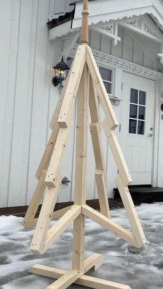 a wooden christmas tree is standing in front of a white building with snow on the ground