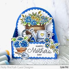 a mothers day card with blue flowers and a watering can on the front, next to some crayons