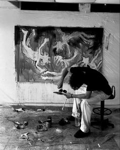 a black and white photo of a man sitting in front of a painting