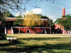 an old red brick building sitting on top of a lush green field next to trees