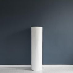 a tall white vase sitting on top of a floor next to a blue painted wall