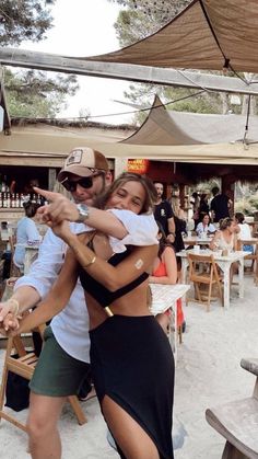 a man and woman dancing in the sand at an outdoor restaurant with people sitting around