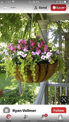 a hanging basket filled with pink and white flowers on top of a porch next to a tree