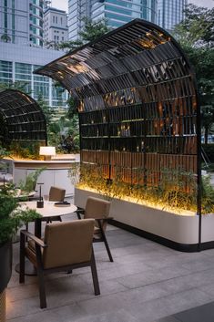 an outdoor dining area with chairs and tables in front of a glass covered wall that has plants growing on it