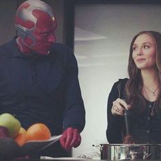 a man and woman standing next to each other in front of a bowl of fruit