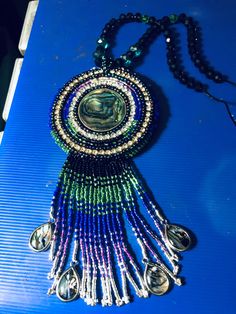 a beaded necklace is sitting on top of a blue surface with silver bells hanging from it