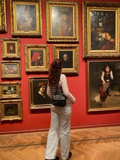 a woman looking at paintings on display in an art museum with red walls and wooden floors