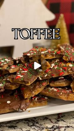 a white plate topped with chocolate covered pretzels and sprinkles next to a christmas tree