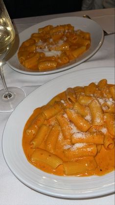 two white plates topped with pasta covered in sauce next to a glass of wine on a table