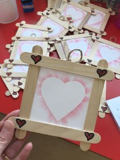 a person holding up a wooden frame with hearts painted on it and several other frames in the background