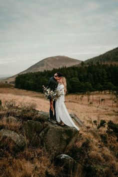 a bride and groom standing on top of a rock in the middle of a field