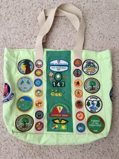 a green tote bag with many different badges on the front and side, sitting on carpet