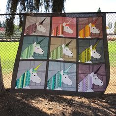 a quilt made to look like unicorns hanging on a chain link fence with trees in the background