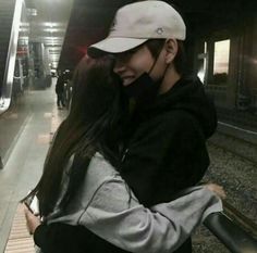 two people hugging each other in front of a train platform with stairs and railings