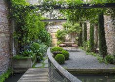 an outdoor garden with stone walls and wooden steps leading to a small pond in the center