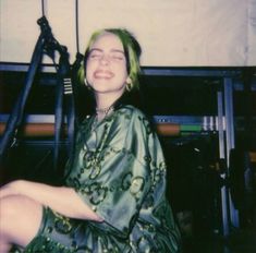 a woman with green hair sitting on the floor in front of a black object and smiling