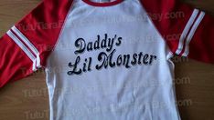 a red and white shirt with the words daddy's lil monster on it sitting on a wooden table