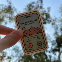 a hand holding up a sticker with the words the mountains are calling