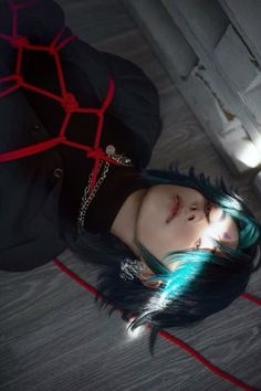 a woman with blue and green hair laying on the floor next to a red rope