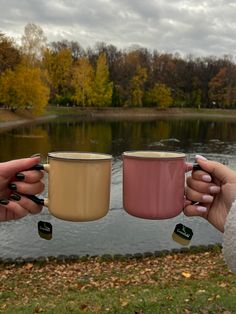 two women holding coffee mugs in front of a lake