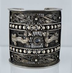 A spectacular cuff. This cuff is circa 1930 and was crafted most likely in French Indochina, modern day Vietnam, Laos, Cambodia, and China. It features an intricate filigree design accented by flowers and dragons. The center of the cuff holds a polished piece of blue/white glass that can easily be replaced by your jeweler. It is INCREDIBLY substantial and weighs 229.5 grams. The cuff measures 3 inches long with an inside measurement of 5 7/8 inches and a 1 1/8 inch opening. There are no hallmark French Indochina, Lapis Ring, Chinese Export, Silver Dragon, Filigree Design, Cz Ring, Vintage Crystal, White Glass, Laos