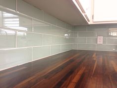 an empty kitchen with wood floors and white tile on the backsplash, in front of a window