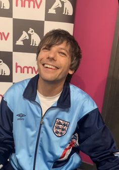 a man sitting in front of a microphone and wearing a blue jacket with an england emblem on it