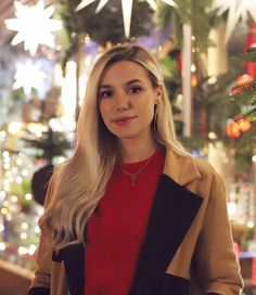 a woman standing in front of a christmas tree wearing a red sweater and black jacket