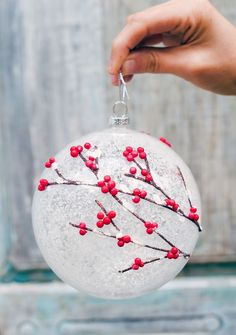 a hand is holding a glass ornament with red berries on it and branches