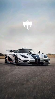 a white and black sports car driving down a road with clouds in the sky behind it