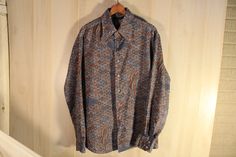 "This is a rare vintage long sleeve men's disco style shirt by Chemi Et Cie. It has all over pattern in blues and browns, no pockets. It has seven plastic buttons down the front, and two on each cuff (one was missing and has been replaced and does not match). 100% Polyester. Tag Size: Large 16 1/2 My Measurements: shoulder- 19 1/2\", pit to pit- 23\", arm- 25\", back- 29 1/2\" Origin: Korea Maker: Chemi Et Cie Year: 1970's Condition: great, pre-owned, miner wear, loose threads, and distress, one Retro Brown Long Sleeve Shirt, Long Sleeve Shirt With Retro Print For Fall, Fall Long Sleeve Shirt With Retro Print, Fall Retro Print Long Sleeve Shirt, Retro Long Sleeve Shirt With Vintage Pattern, Vintage Patterned Long Sleeve Shirt, Long Sleeve Shirt With Retro Print, Vintage Long Sleeve Patterned Shirt, Fitted Long Sleeve Shirt With Retro Print