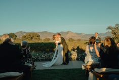 a bride and groom kissing in front of an outdoor wedding ceremony with mountains in the background