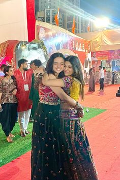 two young women hugging each other on a red carpeted area with people in the background