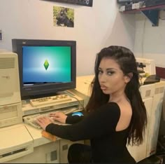 a woman sitting in front of a computer with a monitor and keyboard on top of it