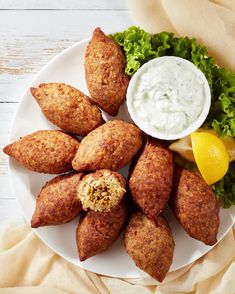 a white plate topped with fried food next to a bowl of ranch dressing and lemon wedges