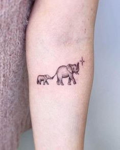 an elephant and her calf tattoo on the left inner arm, with a cross in the middle