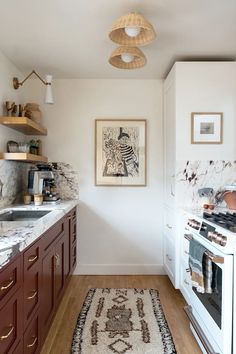 a kitchen with white walls and wooden cabinets, an area rug on the floor and hanging lights over the stove