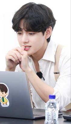 a young man sitting in front of a laptop computer with his chin resting on his hand