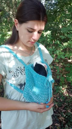 a woman holding a blue crocheted purse in front of her face and looking down