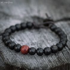 Men's beaded leather mala bracelet. This piece consists of ebony wood beads (8mm), a red wood focal bead, and a coco wood clasp bead, strung on high quality durable brown leather. Ebony wood is mostly black with slight hints of dark brown here and there. I use a bead and loop style clasp which is secure and guaranteed to stay clasped. Rugged, timeless, and durable... as a man's bracelet should be. I use only the highest quality leather cord available on the market. It obtains its color through a Mens Bracelet Diy, Black Beaded Bracelet, Red Beaded Bracelet, Leather Cord Bracelets, Wood Bead Bracelet, Jewelry Design Drawing, Black Beaded Bracelets, Mens Gold Bracelets, Red Wood