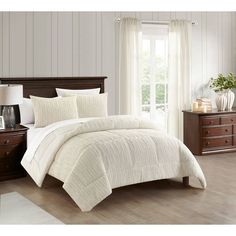 a bed with white comforter and pillows in a room next to a wooden dresser