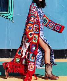 a woman is wearing a colorful crochet dress and cowboy boots while standing in front of a blue wall